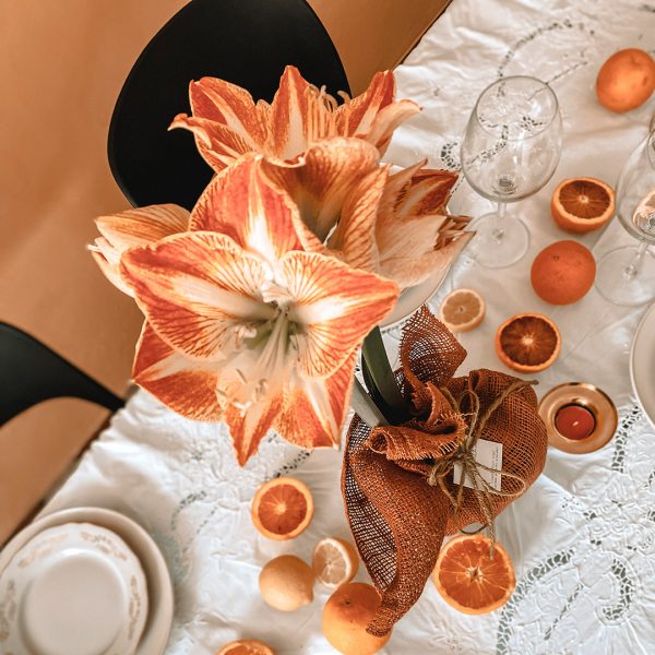 Arrangement mit orangefarbener Amaryllis auf einer gedeckten Tafel