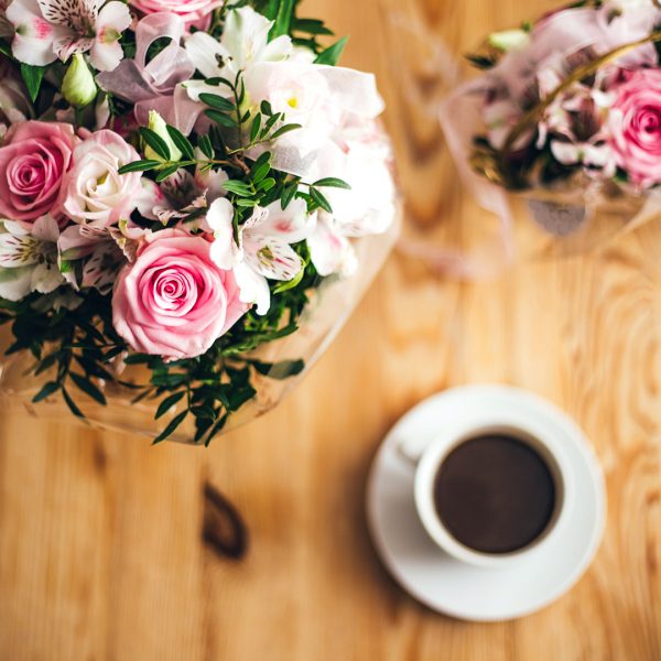 Strauß mit rosa Rosen neben einer Tasse Kaffee