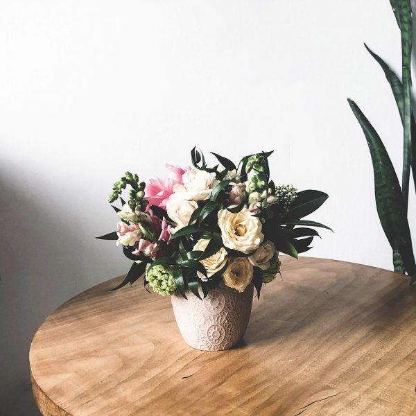 Kleines Blumenarrangement im Keramiktopf auf einem Holztisch